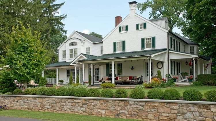 white exterior with covered porch and stone walls whole home remodel by Penn Contractors
